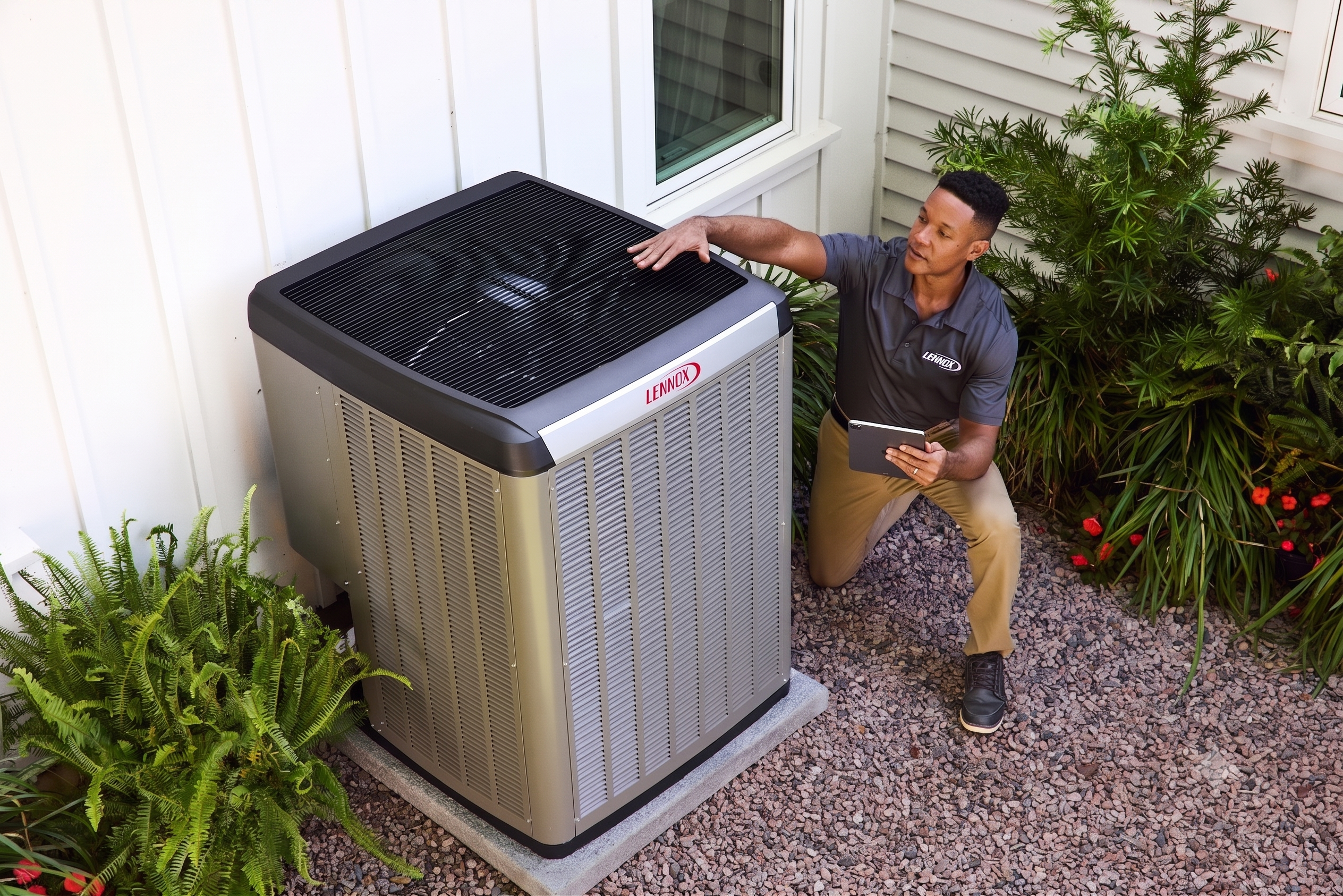 A professional HVAC technician in a Lennox uniform kneels next to a high-efficiency Lennox heat pump AC unit. He uses a tablet for data diagnostics outside a modern white house with gravel and plants. This compressed image is optimized for web performance.