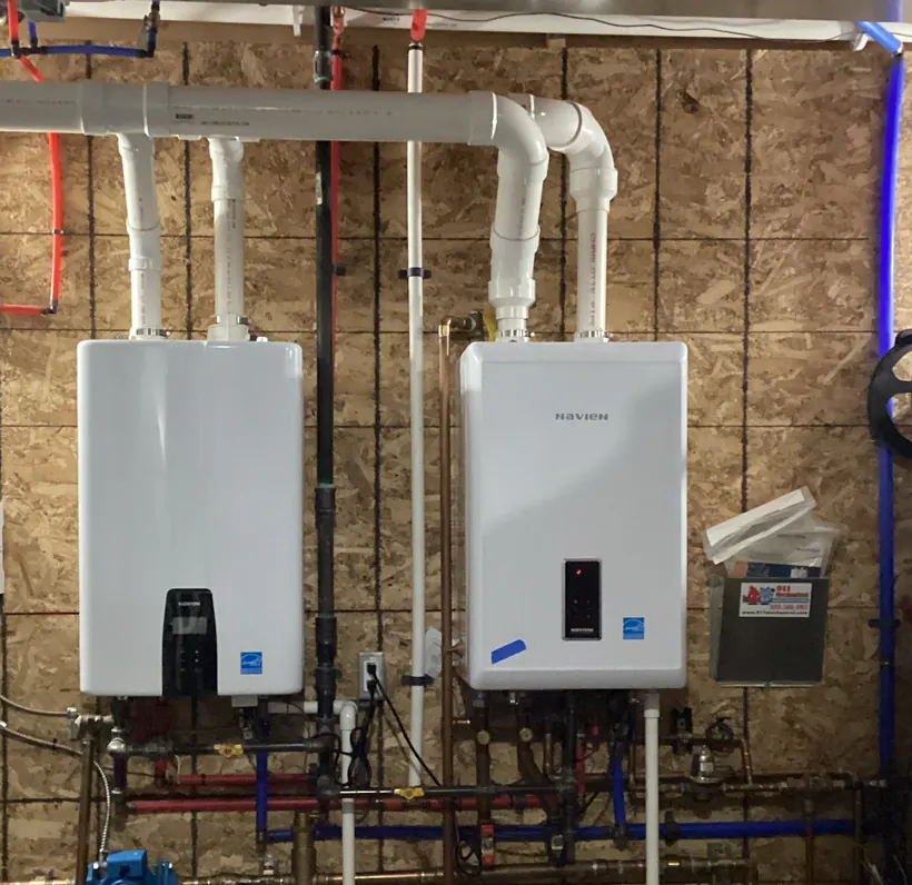 Two wall-mounted Navien units with white vent piping, copper and PEX supply lines and a manifold